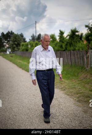 Homme senior marchant sur la route de campagne à côté de l'ancienne clôture en bois Banque D'Images