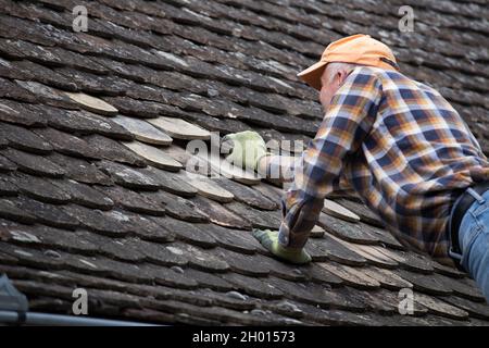 Homme mûr fixant des carreaux simples sur le vieux toit à la maison Banque D'Images