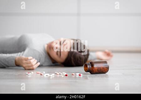 Triste femme millénaire européenne inconsciente couchée sur le sol avec des pilules éparpillées, suicidée à la maison.La femme prend somnifacient, antidépresseur plus Banque D'Images