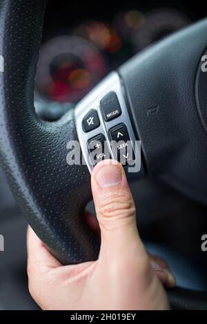 Gros plan de la main mâle maintenant les boutons de commande du volume sur le volant dans la voiture Banque D'Images