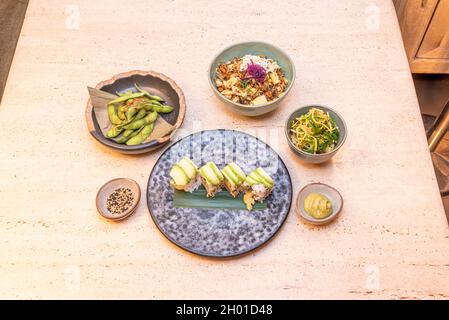 Boîte de légumes d'aliments japonais, rouleau de sushis uramaki avocat, edamame dans les gousses, salade wakame avec nouilles courgettes et salade tofu avec riz et oignon rouge Banque D'Images