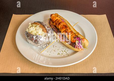 Chien chaud à la saucisse des Caraïbes avec plantain mûr frit et pomme de terre cuite farcie au fromage frais Banque D'Images