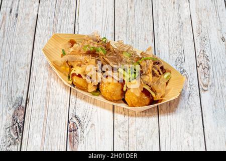 Recette japonaise de boulettes de topus takoyaki cuites avec des tranches de thon séché et de ciboulette hachée dans un panier en bois avec une sauce soja douce Banque D'Images