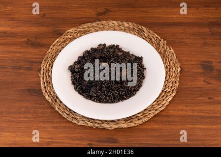 Paella de riz noire avec crevettes et calmars sur une assiette blanche et un trivet en rotin Banque D'Images