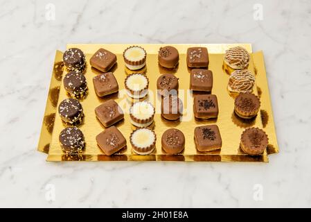 Plateau doré avec assortiment de chocolats artisanaux sur table en marbre blanc Banque D'Images