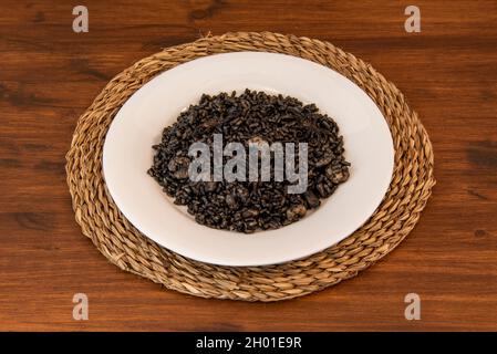 Portion de paella de riz noir avec crevettes et calmar sur une assiette blanche et esparto placemat Banque D'Images