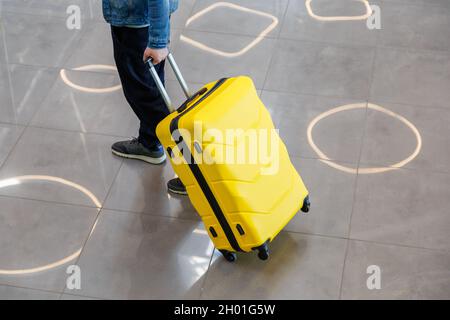 Grande valise jaune dans les mains des hommes sur le chemin de la gare.Un homme traverse l'aéroport et porte une grande valise jaune Banque D'Images