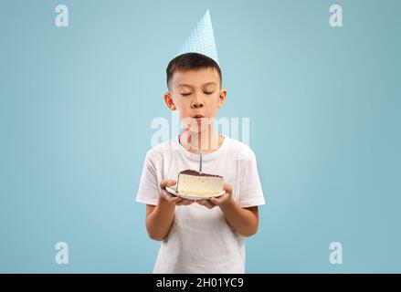 Joli petit garçon asiatique en fête chapeau soufflé bougie sur le gâteau d'anniversaire, petit garçon heureux petit enfant tenue de cadeau doux de jour de B, faire le souhait pendant que vous vous tenez debout Banque D'Images