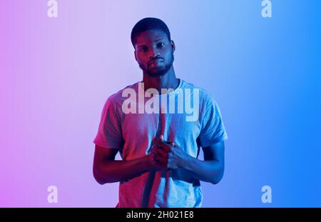 Portrait d'un athlète noir sérieux en t-shirt regardant l'appareil photo en lumière néon.Sportif professionnel motivé posant avec les bras pliés sur sa poitrine.A Banque D'Images