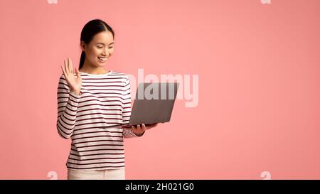 Une femme asiatique joyeuse qui fait un appel vidéo avec un ordinateur portable, qui agite la main à la webcam, une jeune femme coréenne amicale saluant quelqu'un, appréciant la communication en ligne Banque D'Images