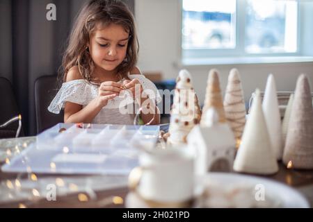 Jolie petite fille avec cheveux bouclés faire des métiers et décorer le cône de sapin de Noël avec des boutons. Banque D'Images