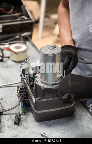 main d'une personne réparant un objet métallique moderne qui se trouve sur son lieu de travail, restauration de l'équipement en atelier Banque D'Images