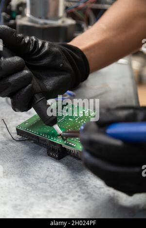 gros plan sur la main d'une personne tenant une machine à souder pour réparer une puce, la technologie et la restauration de l'équipement en atelier, outils professionnels Banque D'Images