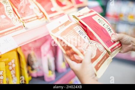 WUHAN, CHINE- SEP 22, 2021: Main de femme en gros plan en choisissant la collation qui prête à manger sur l'étagère au supermarché local. Banque D'Images