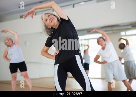 Femme active et mature qui s'étire pendant l'entraînement de groupe Banque D'Images