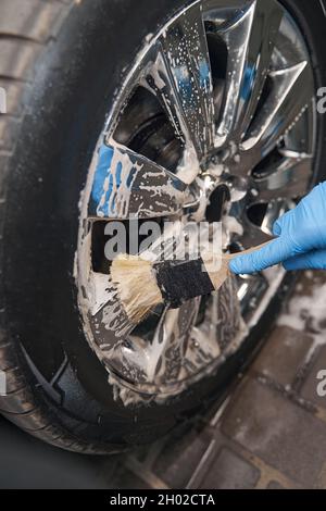 L'agent de centre de nettoyage nettoie les roues de la voiture à l'aide d'une brosse Banque D'Images