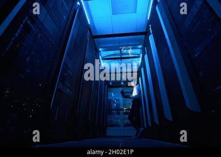 Technicien de serveur travaillant avec un ordinateur portable dans un passage de l'installation de données Banque D'Images