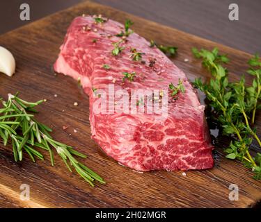 Steak de stripine cru au romarin, au thym et à l'ail sur une planche à découper en bois. Banque D'Images