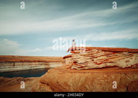 Femme assise sur une falaise.Falaises de grès, lac Powell et ciel nuageux.Explorer les chaînes, Glen Canyon, page, Arizona Banque D'Images