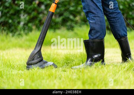 un travailleur utilisant une tondeuse à ficelle pour couper de l'herbe à la maison Banque D'Images