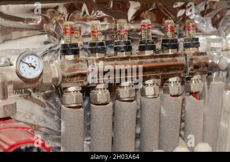 Collecteur de chauffage au sol installé sur le mur. Tuyaux isolés d'alimentation en eau et de circulation. Pompe à eau électrique rouge. Thermomètre. À l'intérieur de la pièce. Banque D'Images