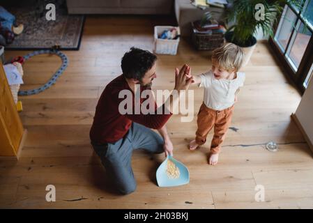 Vue de haut en avant du père haut de cinq avec petit fils après avoir balayé à la maison, le concept de corvées quotidiennes. Banque D'Images