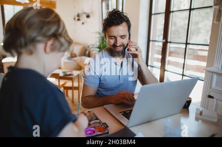 Père adulte moyen avec petit fils travaillant à l'intérieur à la maison, peinture des images et le concept de bureau à la maison. Banque D'Images