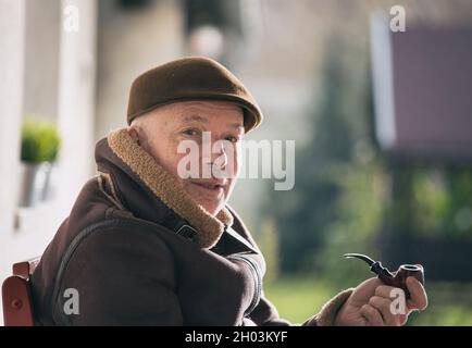 Portrait de l'homme mature assis dans le jardin en hiver et fumant la pipe Banque D'Images