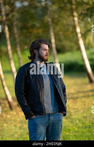 Jeune homme barbu debout et regardant à distance sur un fond d'arbres d'automne colorés Banque D'Images
