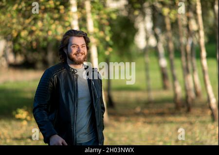 joyeux jeune homme barbu souriant et regardant la caméra contre l'automne couleur arbres arrière-plan Banque D'Images