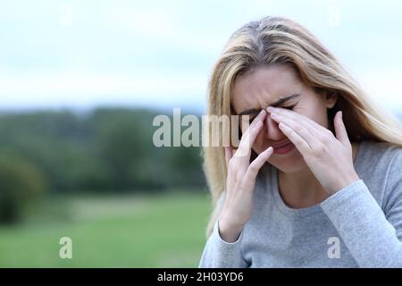 L'adolescent rayant les yeux qui démangent avec les deux mains à l'extérieur dans un champ Banque D'Images