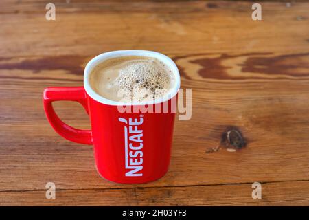 Mug rouge Nescafé, rempli de café chaud, sur fond de bois Banque D'Images