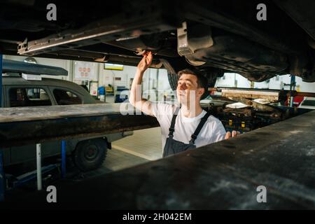 Portrait de tir moyen d'un beau professionnel de mécanicien de voiture en uniforme debout dans la fosse d'inspection et de travail avec l'outil. Banque D'Images