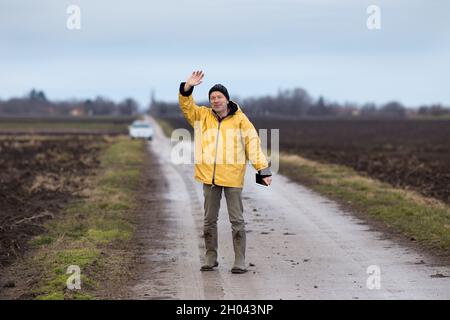 Agriculteur mature avec une tablette debout à côté du champ et en agitant la main en hiver Banque D'Images