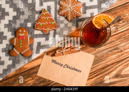 vue de dessus des biscuits au pain d'épice sur la couverture près de la carte de vœux avec lettrage joyeux noël et une tasse de thé sur une surface en bois Banque D'Images