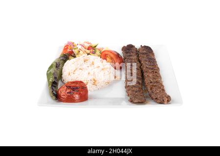 Turc adana kebab. Avec légumes, riz dans une assiette de service en porcelaine sur fond blanc. adana sis, adana kebap, kiyma kebap Banque D'Images