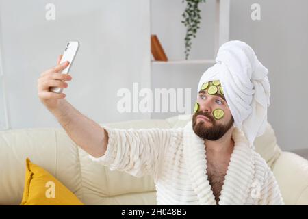 Homme barbu tenant des tranches de concombre sur le visage. Spa à la maison, soins du corps et de la peau pour homme concept. Banque D'Images