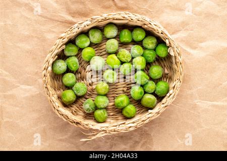 Plusieurs pois verts surgelés dans une assiette de paille, gros plan, sur papier brun, vue de dessus. Banque D'Images