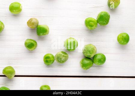 Plusieurs pois verts surgelés, gros plan, sur une table en bois blanc, vue de dessus. Banque D'Images