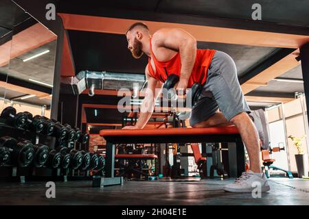 Un jeune homme sportif barbu s'entraîne avec des haltères dans la salle de gym.Vue de dessous.Le concept d'un style de vie sportif et de la forme physique. Banque D'Images