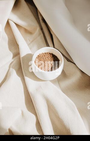 Café moulu dans un petit bol blanc sur un fond beige isolé.Concept café 2022. Banque D'Images