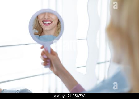 Femme regardant son beau sourire blanc sain dans le miroir dentaire reflet, méconnaissable jeune femme heureuse vérifiant les résultats du traitement Banque D'Images