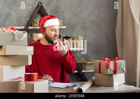 Cadeaux de Noël et de vacances service de livraison pour les petites entreprises.Un homme dans un chapeau de Père Noël assis entre des boîtes avec des cadeaux pour la nouvelle année Banque D'Images