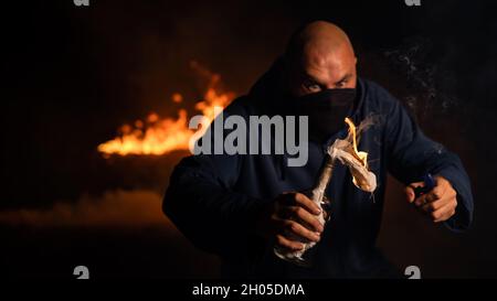 Un homme masqué tient une bouteille brûlante. Cocktail Molotov. Banque D'Images