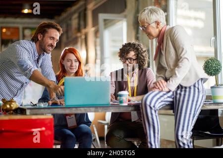 des patrons satisfaits montrant aux jeunes adultes de nouvelles idées d'affaires sur un ordinateur portable, souriant, Banque D'Images