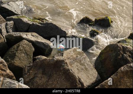 Une boule de plage colorée perdue attrapée dans les rochers de défense de la mer à Lowestoft front de mer Banque D'Images