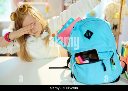 école moderne fille avec des livres de travail et sac à dos bleu en sweat-shirt blanc faisant un geste de dabuvant à la maison par jour ensoleillé. Banque D'Images
