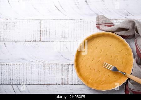 Pâte à cuire quiche, tarte ou tarte en céramique prêt à cuire sur une serviette de cuisine sur fond blanc en bois de planche rustique ancien. Vue de dessus, c Banque D'Images