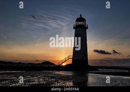Le soleil se couche derrière les dunes contre le phare de point of Ayr à Talacre, au nord du pays de Galles. Banque D'Images