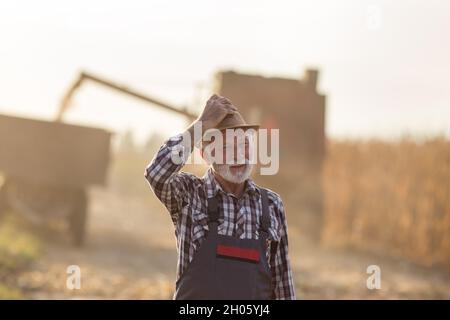 Portrait d'un agriculteur âgé fatigué devant la remorque de chargement de la moissonneuse-batteuse au coucher du soleil Banque D'Images